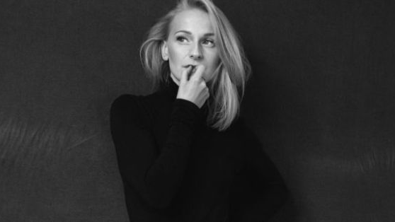 Black and white photo of a young woman, with blonde hair, dressed in black. The woman looks thoughtfully to the side.