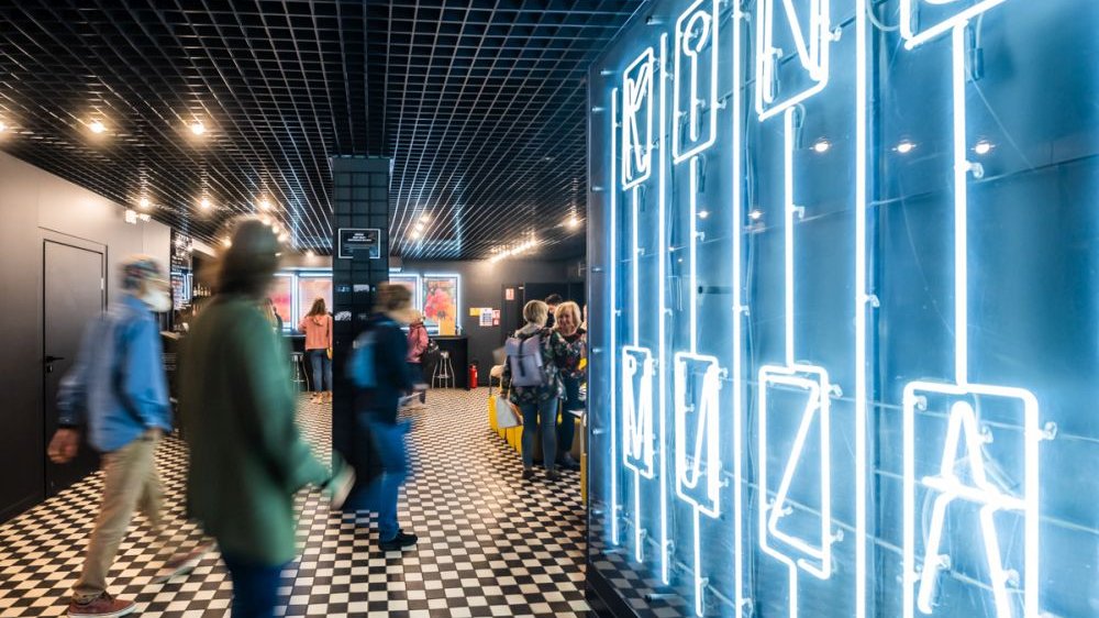 People in the cinema hall, a bright neon sign on the right.