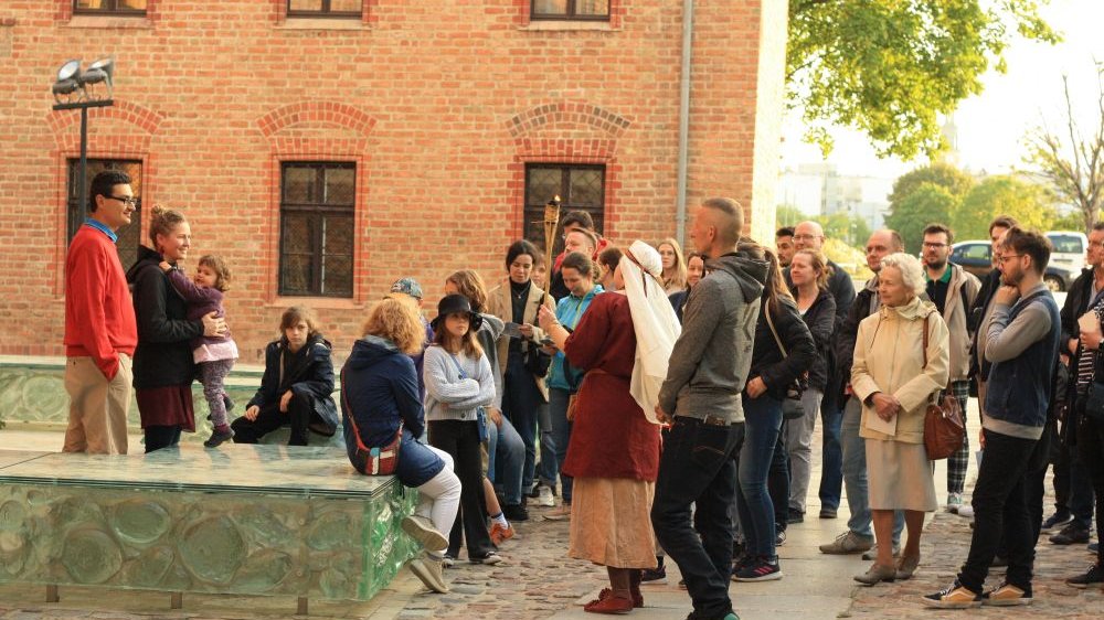 A group of people listening to a guide during a tour. A building wall in the background.