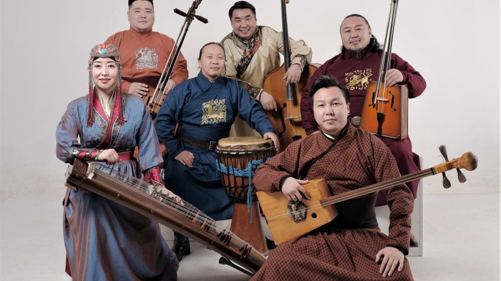 Five men and one woman in traditional Mongolian folk costumes pose with instruments.