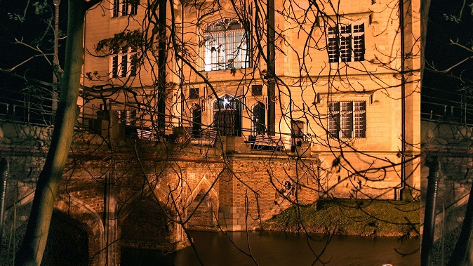 An illuminated building with a brick bridge leading to it. Water under the bridge.