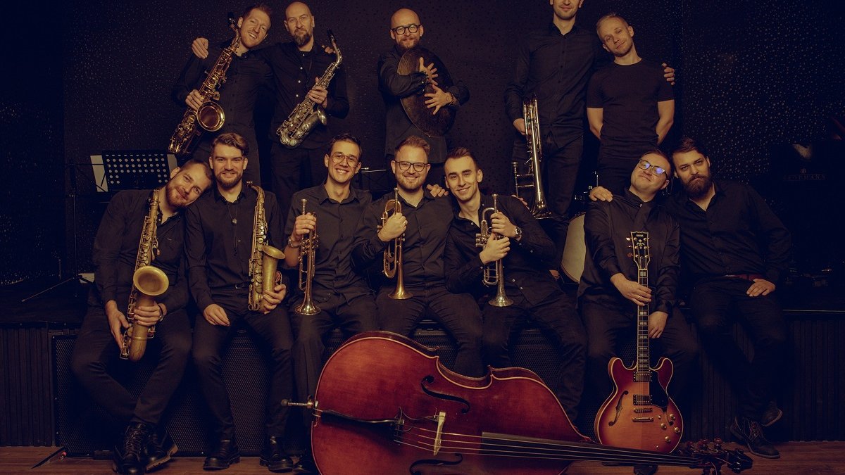 Colourful photo of 12 men in two rows, most of them are holding musical instruments. In front of them a double bass laying on the floor.