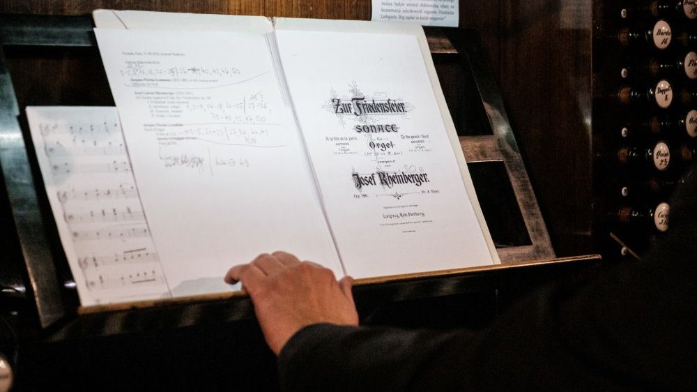 The musician opens his sheet music to the title page, where the title of the piece being played and the name of the artist (in German) are written in Gothic script. The musician's hand is visible next to the music stand.