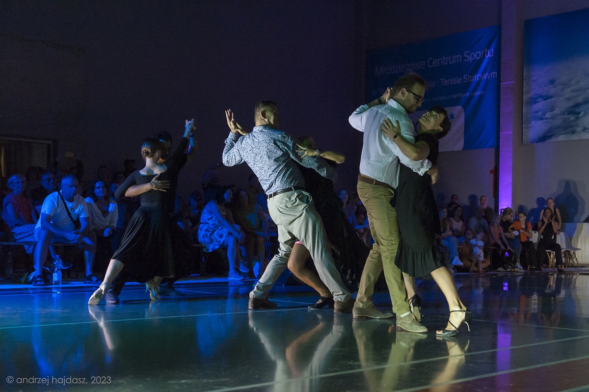 Photo of three dancing couples. In the background the audience - people sitting on chairs and watching the show. - grafika artykułu