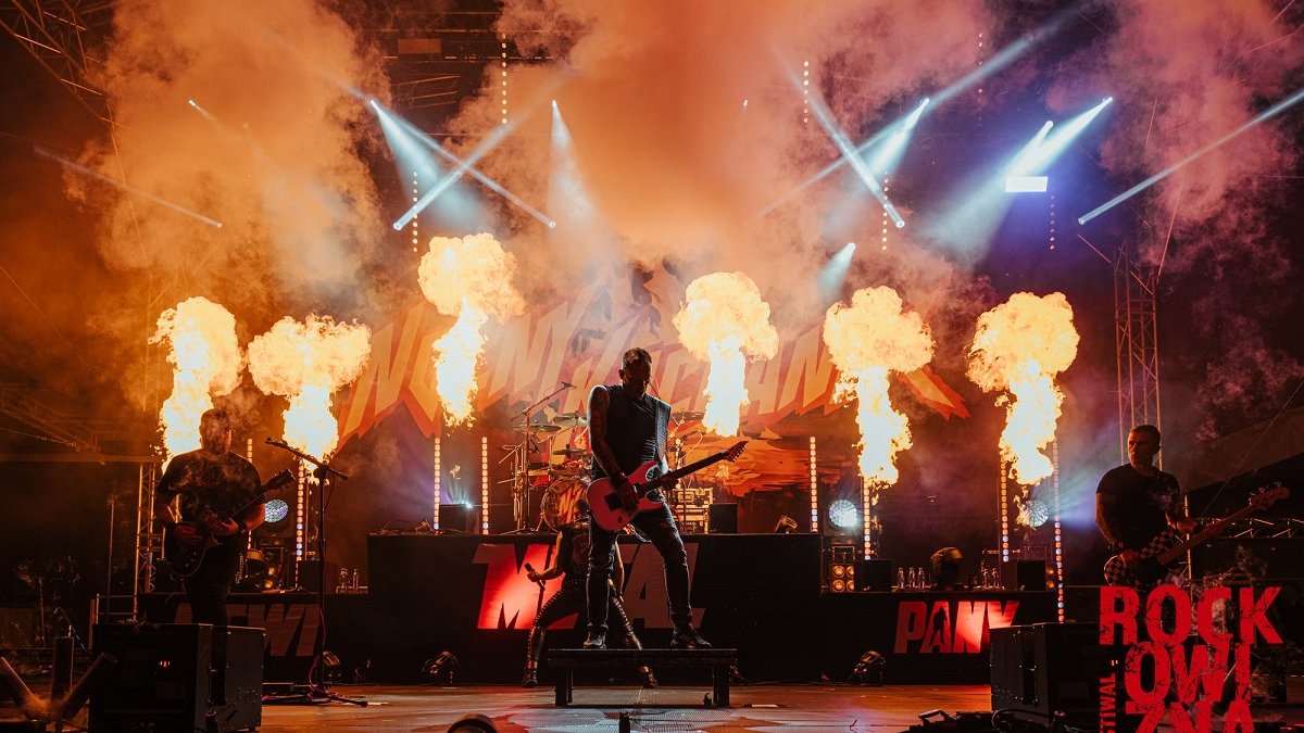 A rock band on stage. Behind the musicians, flames and a lot of smoke.