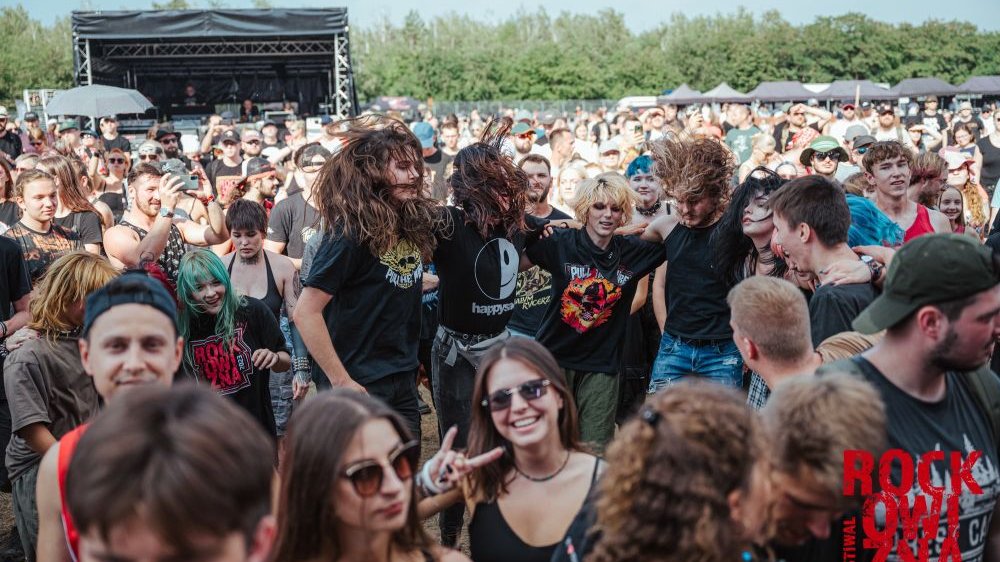 Young people having fun in front of an outdoor stage. Most of them are wearing black clothes.