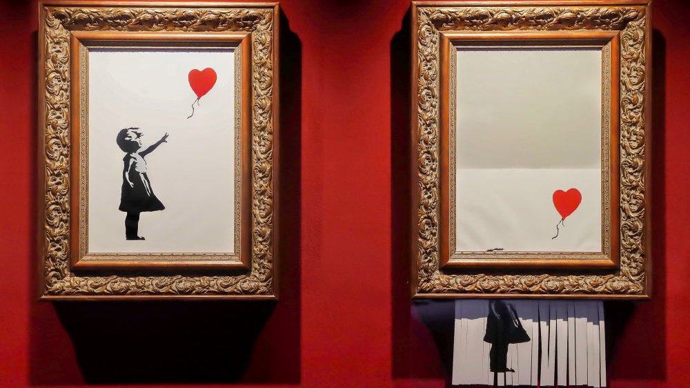 The same picture of a little girl releasing a heart-shaped balloon, placed in gold frames hanging on a red wall. On the left the picture is intact, on the right it is partially destroyed by a paper shredder.