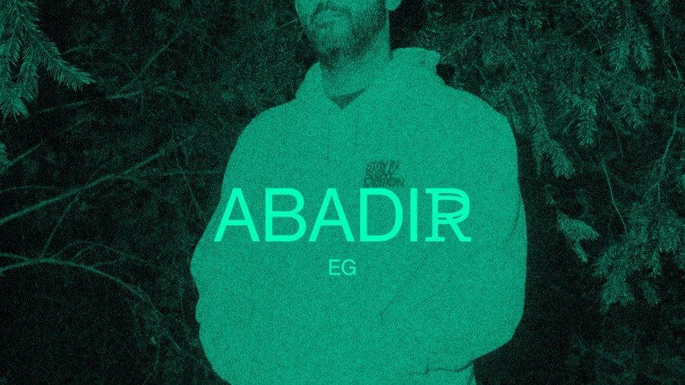 Green and black photo of a man in a sweatshirt, with his hands in his pockets. In the middle - the inscription "Abadir".