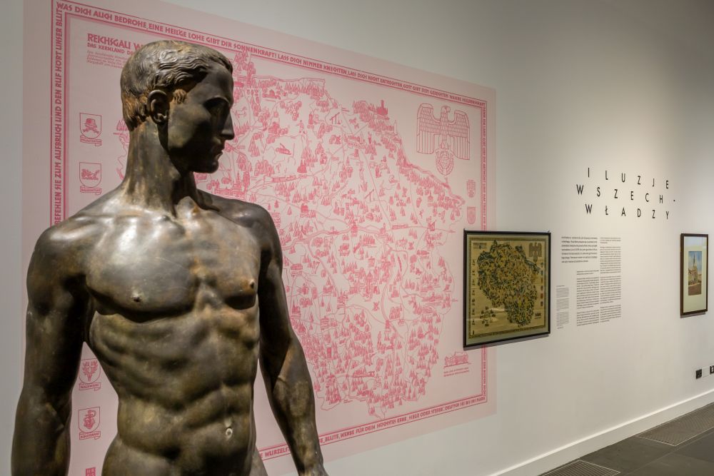 In the foreground there is a sculpture of a naked man, in the background on the wall there is, among other things, a pink city map. - grafika artykułu