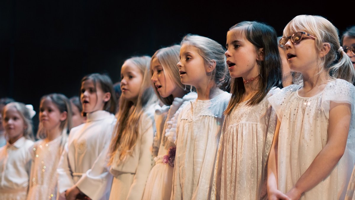 Photo of a few-year-old girls in white dresses, standing in a row and singing.