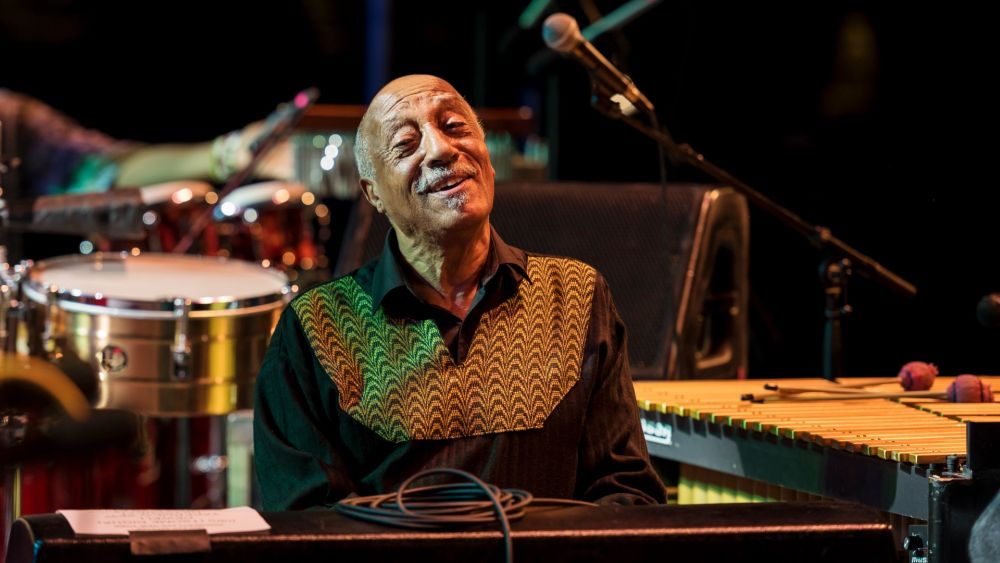 A photo of a smiling musician with musical instruments behind him. - grafika artykułu