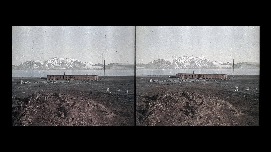 Empty space with a single-story long building, in the background water and a mountain partially covered with snow.