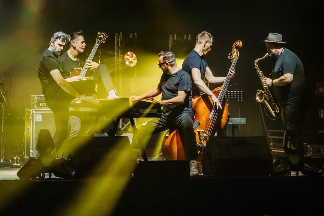Photo of music players: five men playing their instruments such as guitar, key board, double bass and saxophone. - grafika artykułu