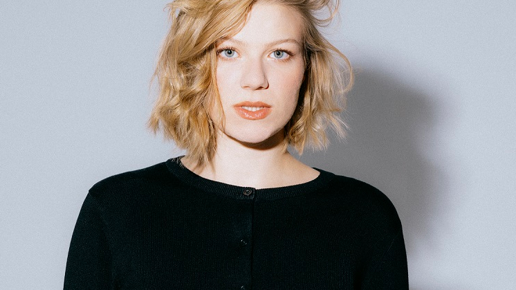 Young woman in black clothes standing and looking straight ahead. Grey background.