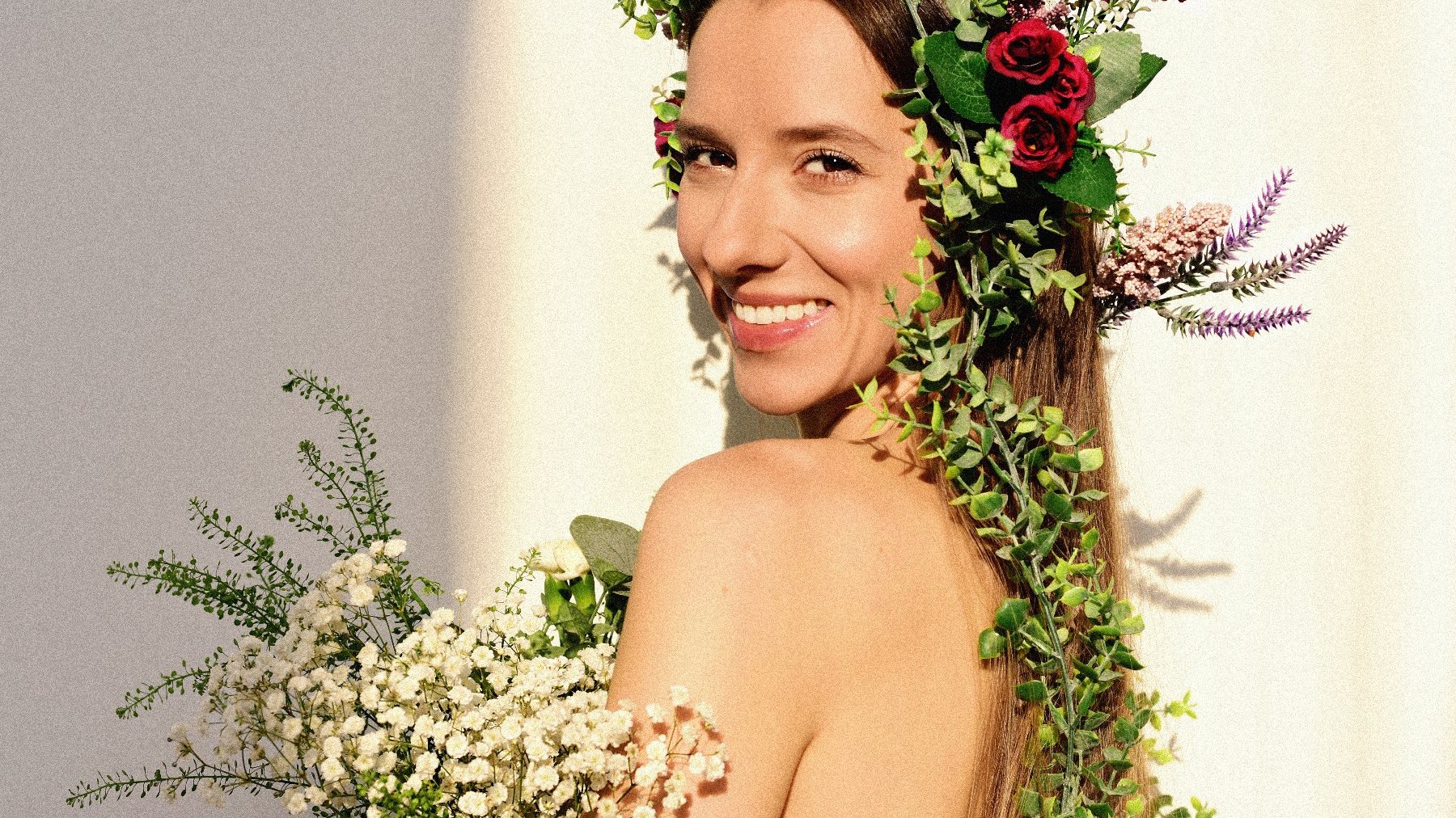 Smiling girl with herbaceous flowers in her hair and with a bouquet in her hands.