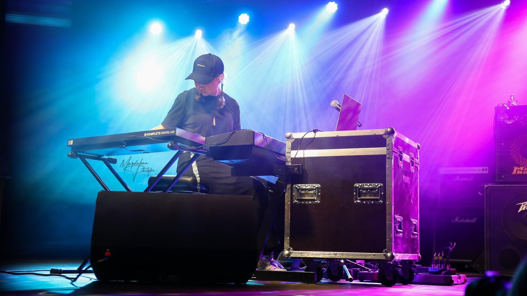 A young girl with pigtails plays keyboards on stage. The stage is lit in blue and purple.