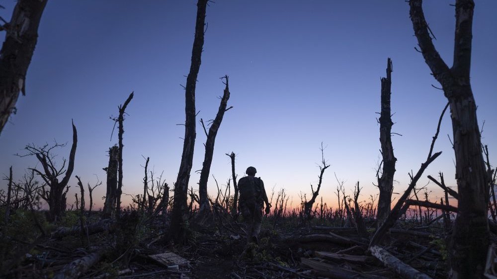 Ukrainian soldier in a shell-ravaged forest during sunset.