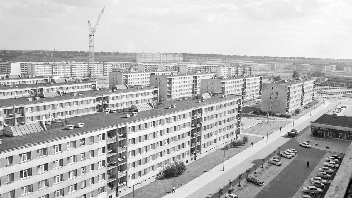 A black and white photo of a housing estate. A car park is in the foreground.