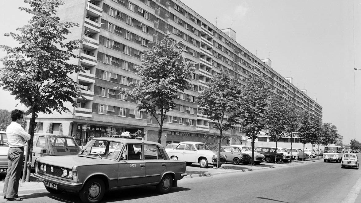 Black and white photo of a residential block, a street and several cars in the foreground.