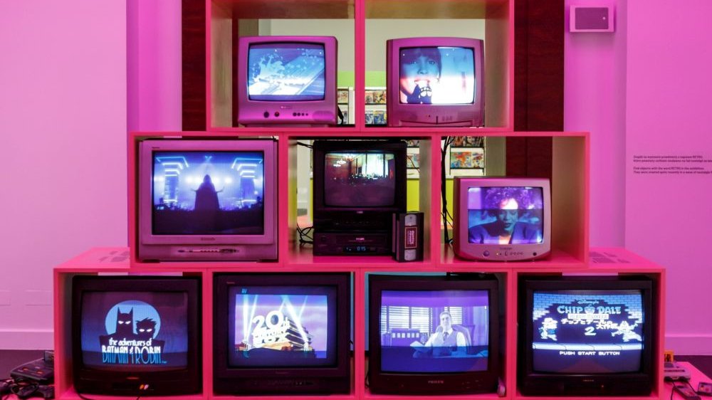There are nine small TVs in total in several rows. Some show a fragment of Whitney Houston music video, another the "Batman and Robin" cartoon, another the 20 Centuries logo, and another Lord Vader.