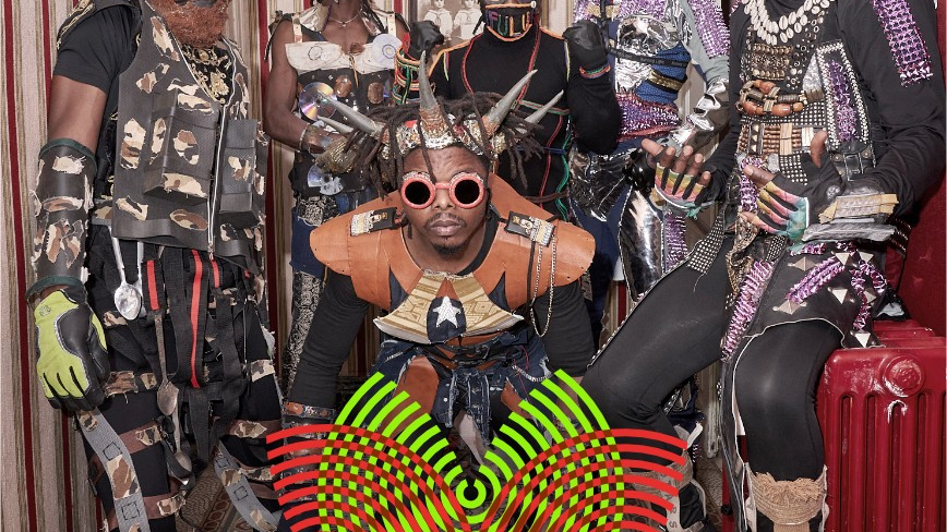 Six black men wearing fancy costumes, masks, and headbands/horns made of various materials.
