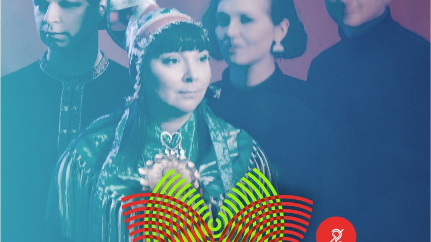 The singer has long black hair, a green embroidered suit and a red Icelandic hat. Behind her are three members of her band.