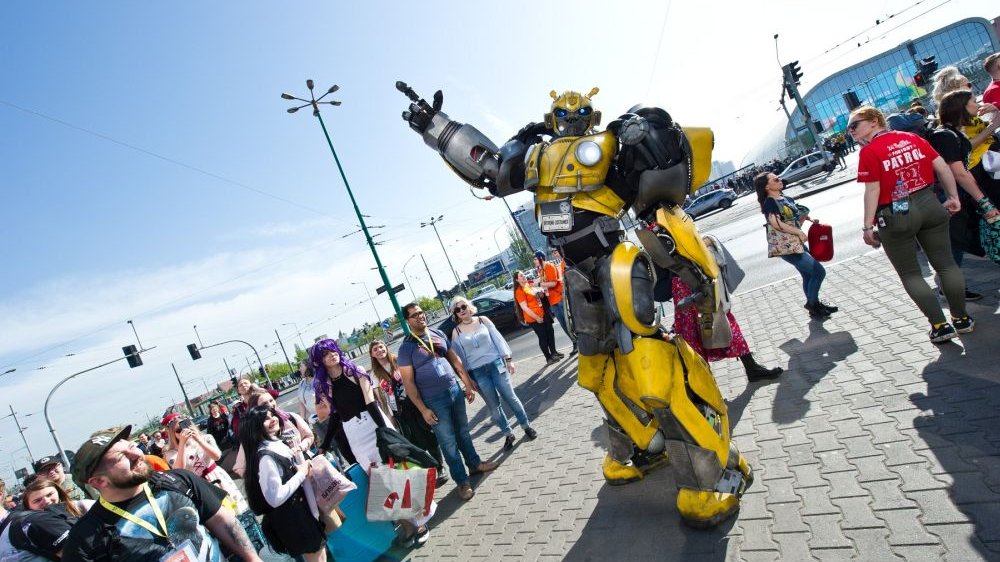Pyrkon participant in a yellow Transformer costume, on the street, surrounded by people.