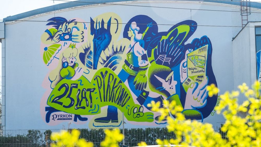 Green and blue mural of Pyrkon on the wall of the building.