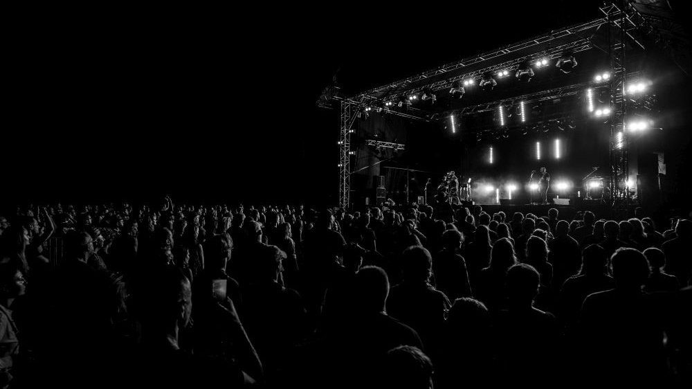 Night concert on an outdoor stage, the stage is only dimly lit, the audience stands in front of it.