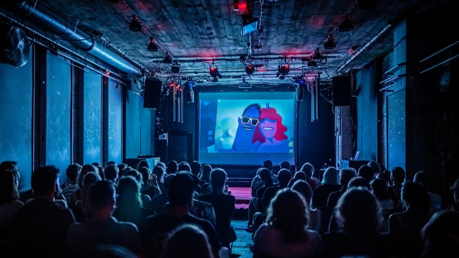 A darkened hall, full of viewers. An animated film is displayed on the screen.
