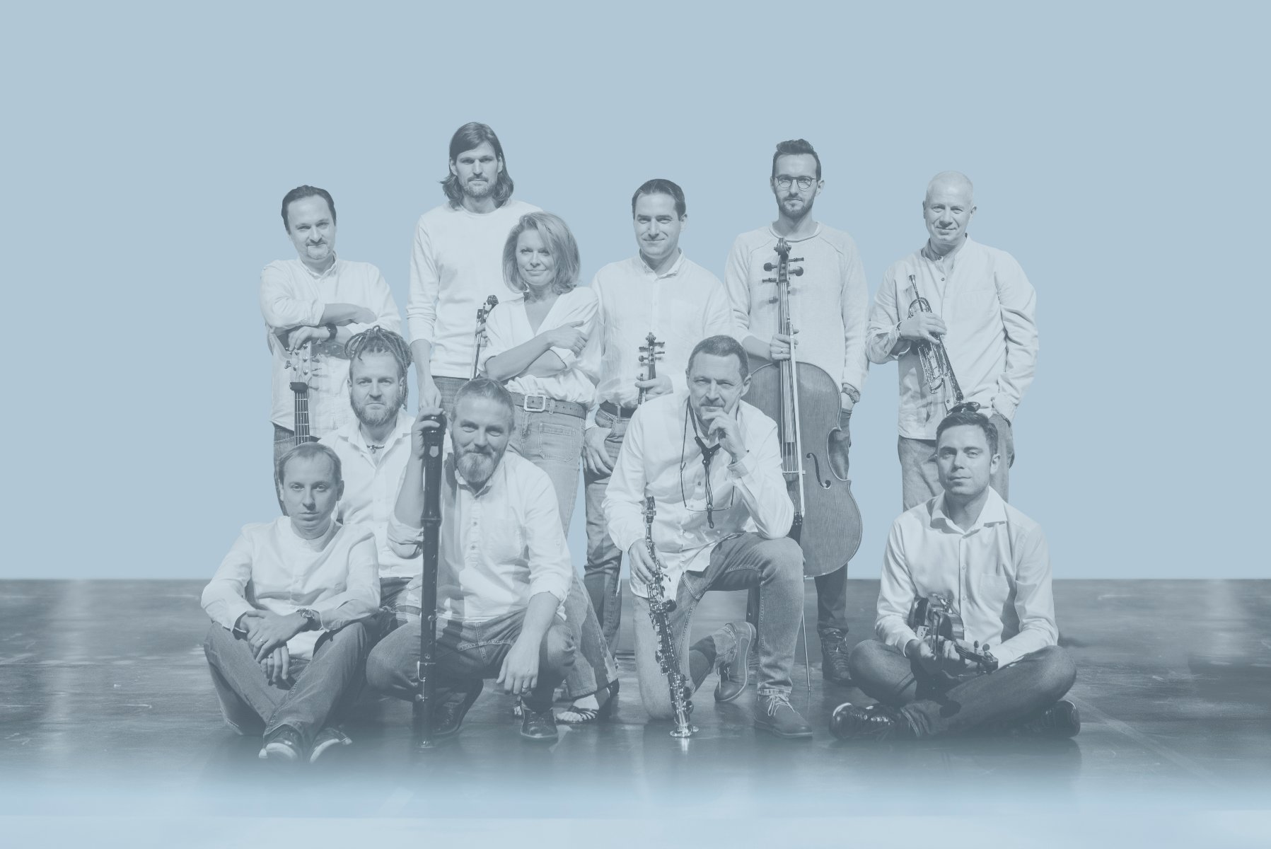 A white and blue photograph of musicians: one woman and ten men, some holding musical instruments. - grafika artykułu