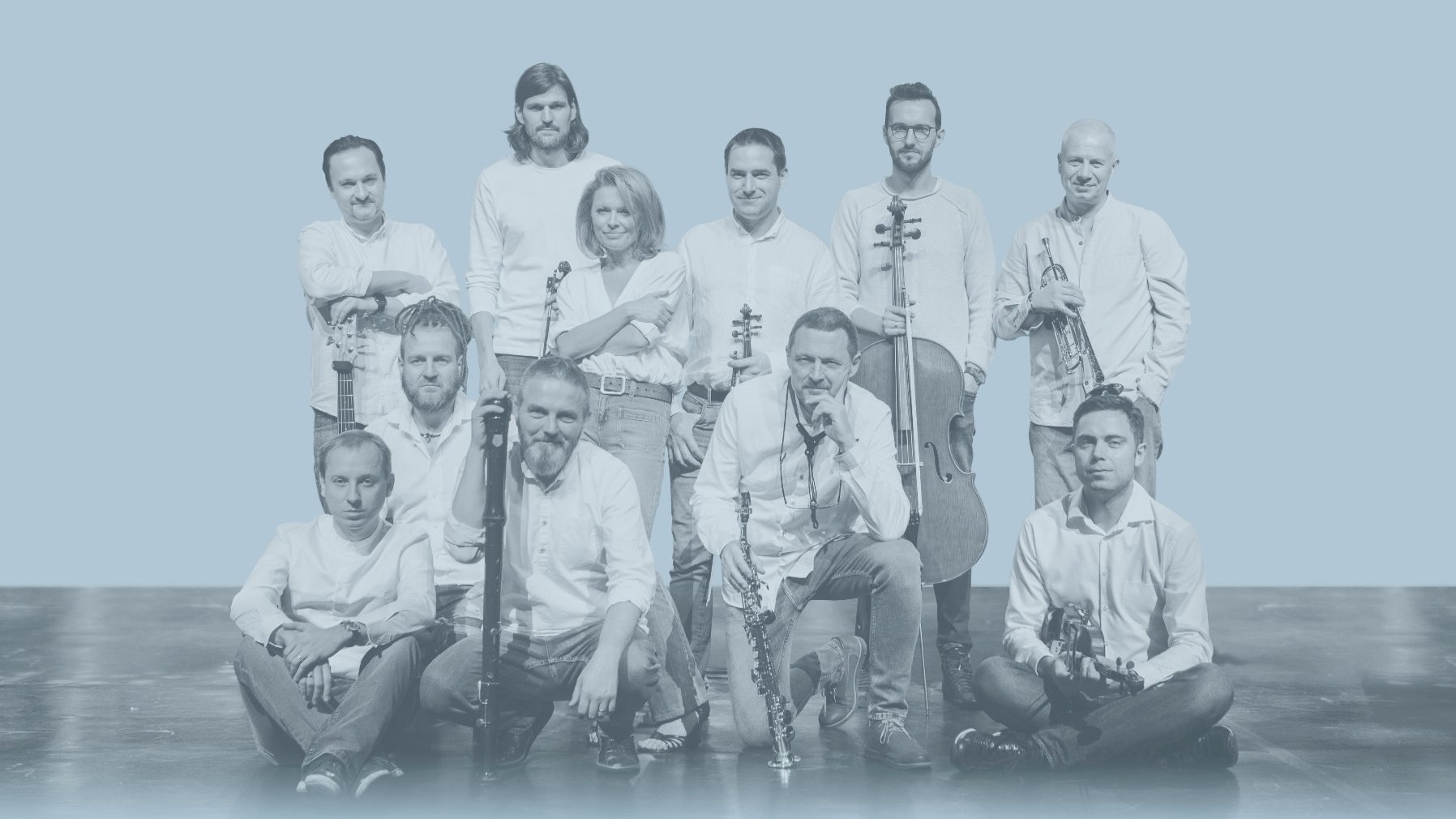 A white and blue photograph of musicians: one woman and ten men, some holding musical instruments.