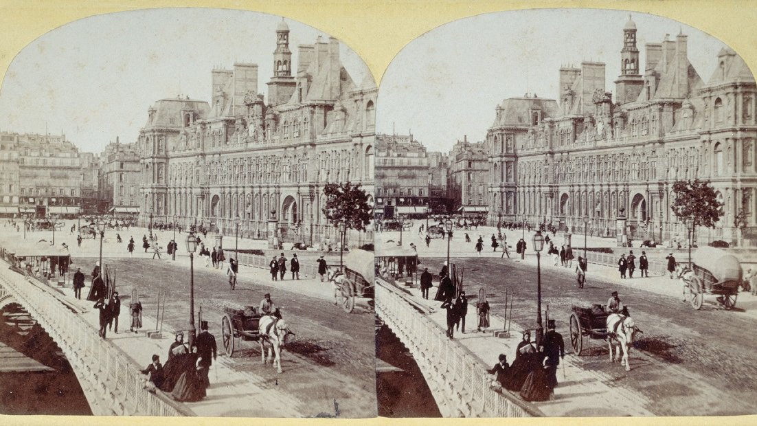 Stereo photography showing a street lined with horse-drawn carriages and people strolling. Across the street there is a stately building.