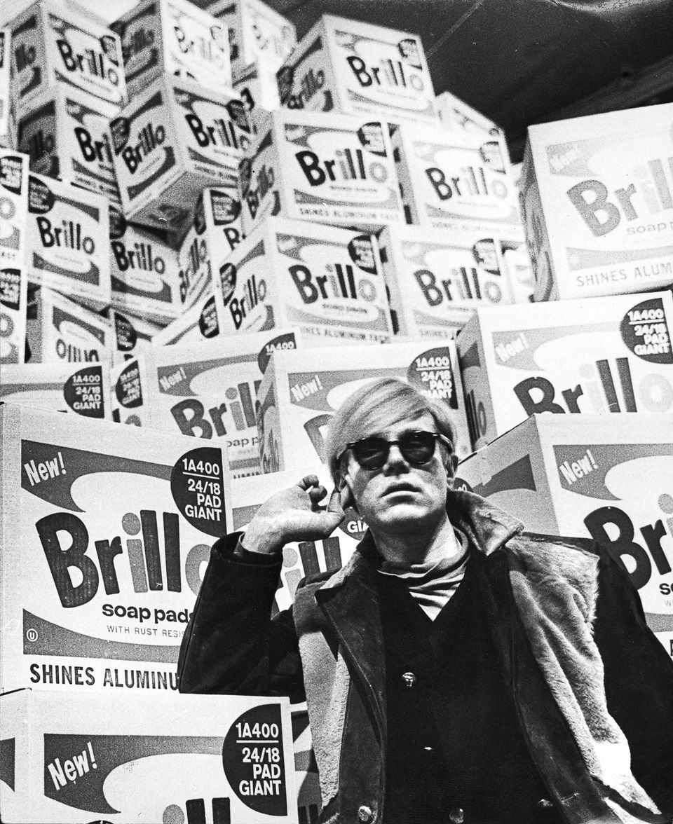 Black and white photo of a person in front of boxes of soap pads. The person is holding their hand to his or her ear. - grafika artykułu