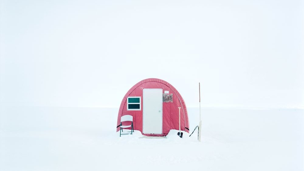 A red tent is pitched in the snow, with a chair in front of it.