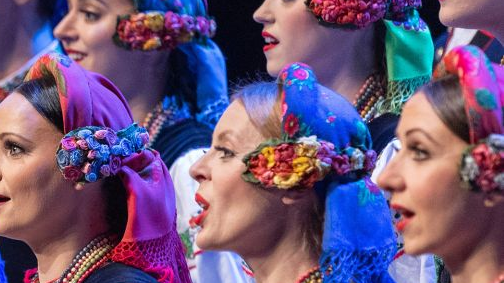 Three singing women in rich folk costumes.
