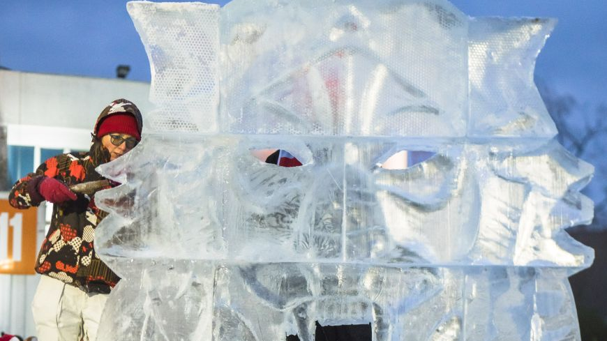 An ice sculpture of an animal's head, with a woman grinding ice behind it.