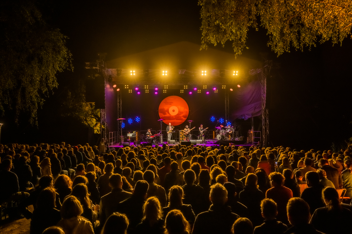 The stage is in semi-darkness, with musicians on it and an audience in front of the stage. - grafika artykułu