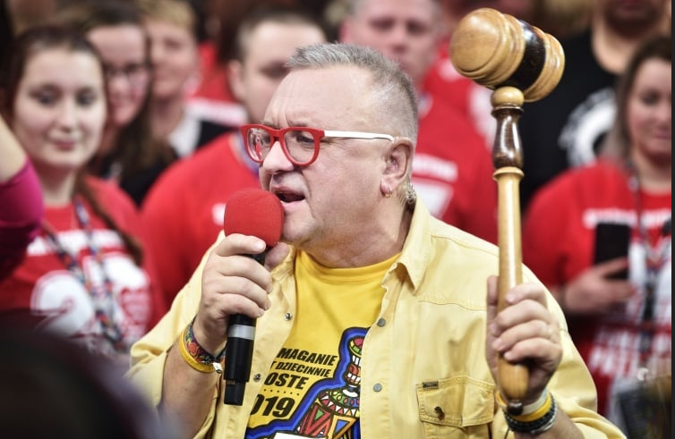 Jurek Owsiak with a microphone on stage during the final moments of the auction, holding the auction hammer in his hands. - grafika artykułu