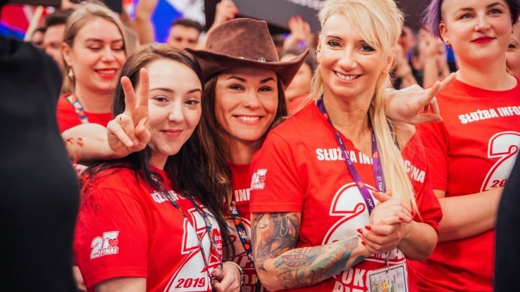 A group of girls in red t-shirts of the WOŚP information service smile at the camera.