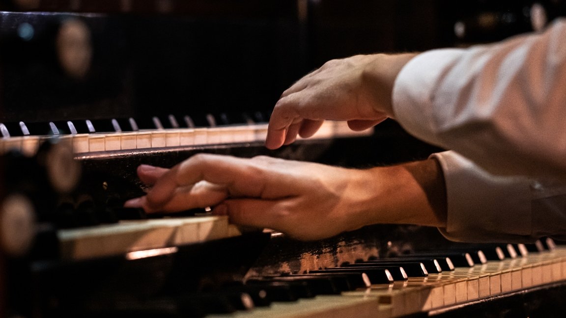 The photo shows a musician's hands on a pipe organ keyboard