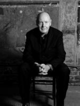 Black and white photo of the conductor - a sitting man with his hands folded