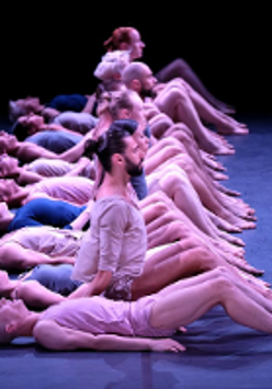 Photo from the performance: dancers in a row, some of them sitting on floor, some of them lying.