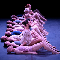 Photo from the performance: dancers in a row, some of them sitting on floor, some of them lying.