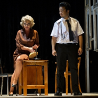 Photo from the performance: a woman sitting on a desk and a man standing next to her.