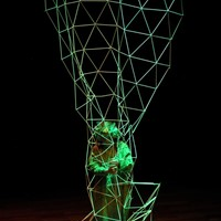 Photo presents an actor in green garment inside a green openwork wire construction on black background