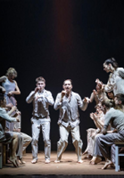 Photo of a group of dancers, some of them standing and some of them sitting on stools.