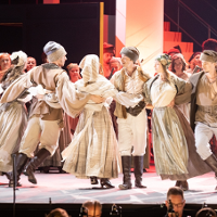 A group of dancers in folk costumes dance in a circle.