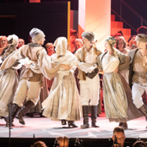 A group of dancers in folk costumes dance in a circle.