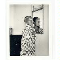 Black and white photo of a woman standing by the wall. Her figure is reflected in the mirror